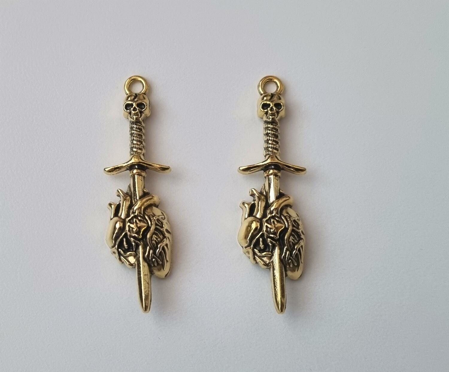 2 st guldfärgade dödskallesvärd genom ett hjärta,. Berlocker / charms