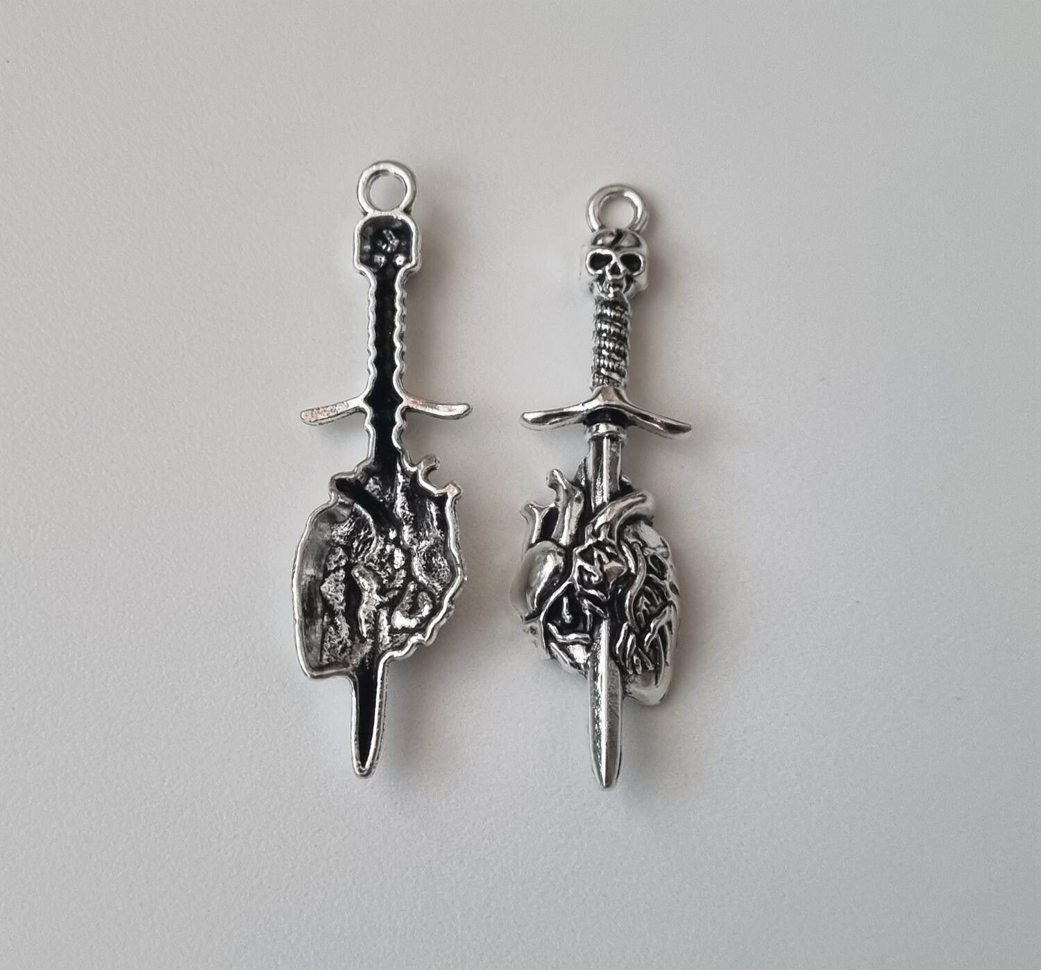 2 st silverfärgade dödskallesvärd genom ett hjärta,. Berlocker / charms