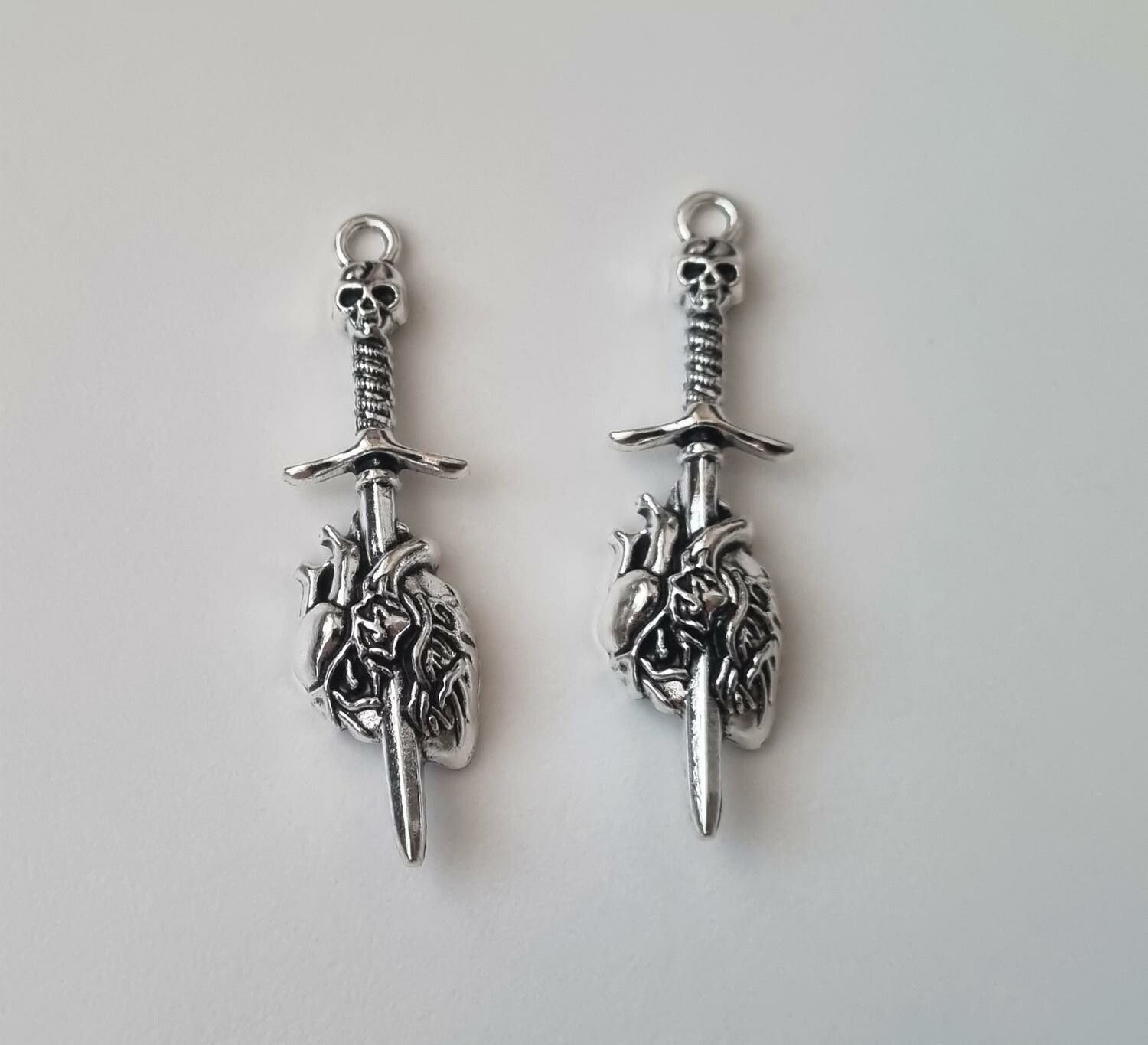 2 st silverfärgade dödskallesvärd genom ett hjärta,. Berlocker / charms