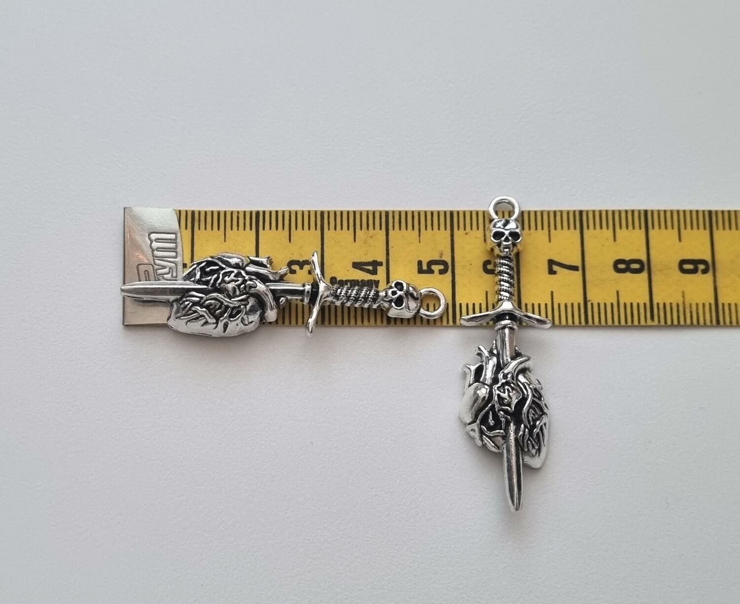 2 st silverfärgade dödskallesvärd genom ett hjärta,. Berlocker / charms