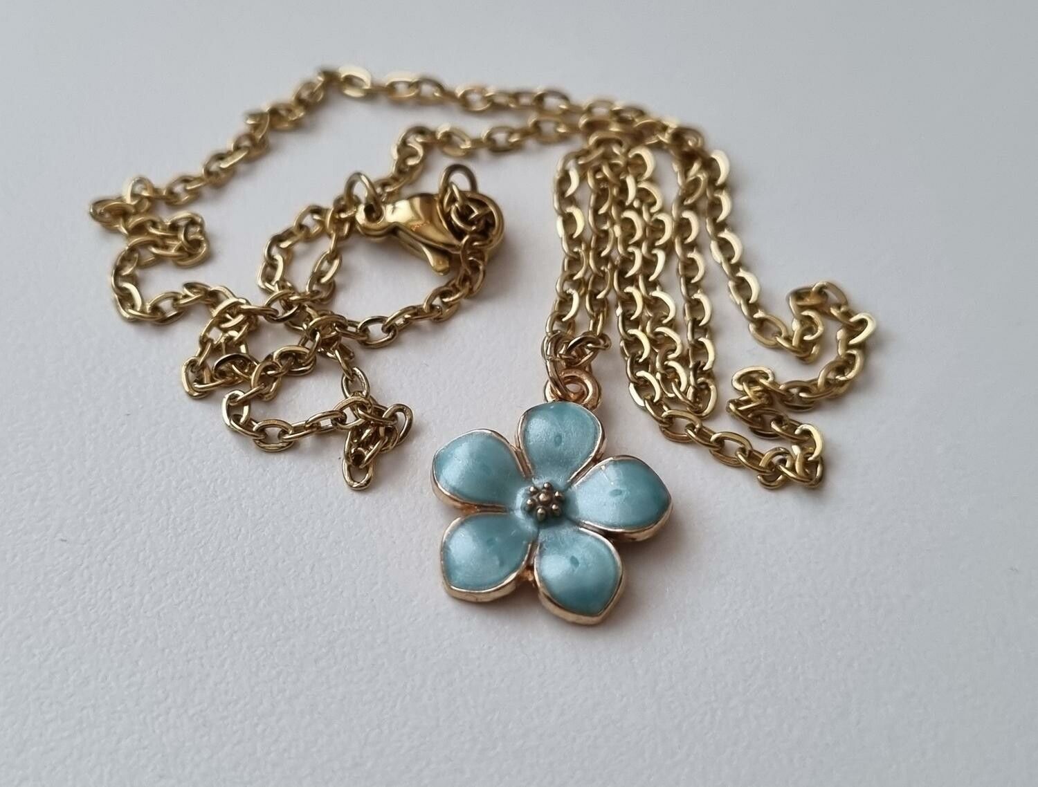 Guldfärgat halsband med en turkos blomma