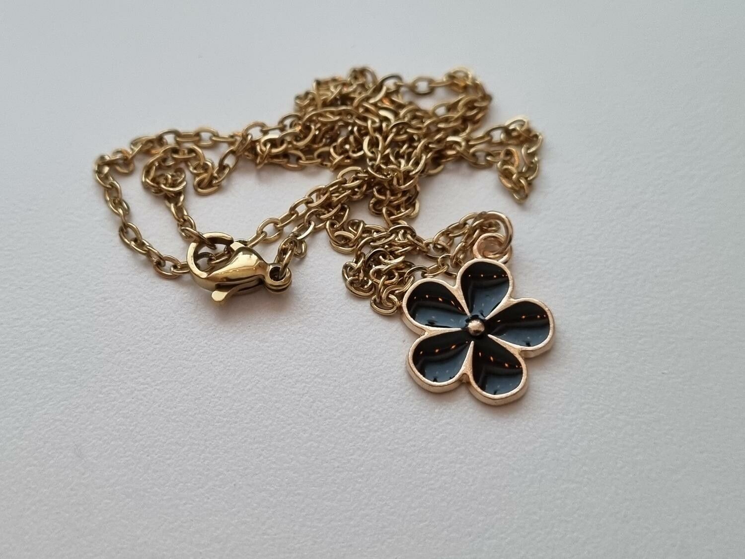 Guldfärgat halsband med en svart blomma / blomberlock