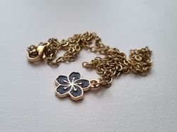 Guldfärgat halsband med en svart blomma