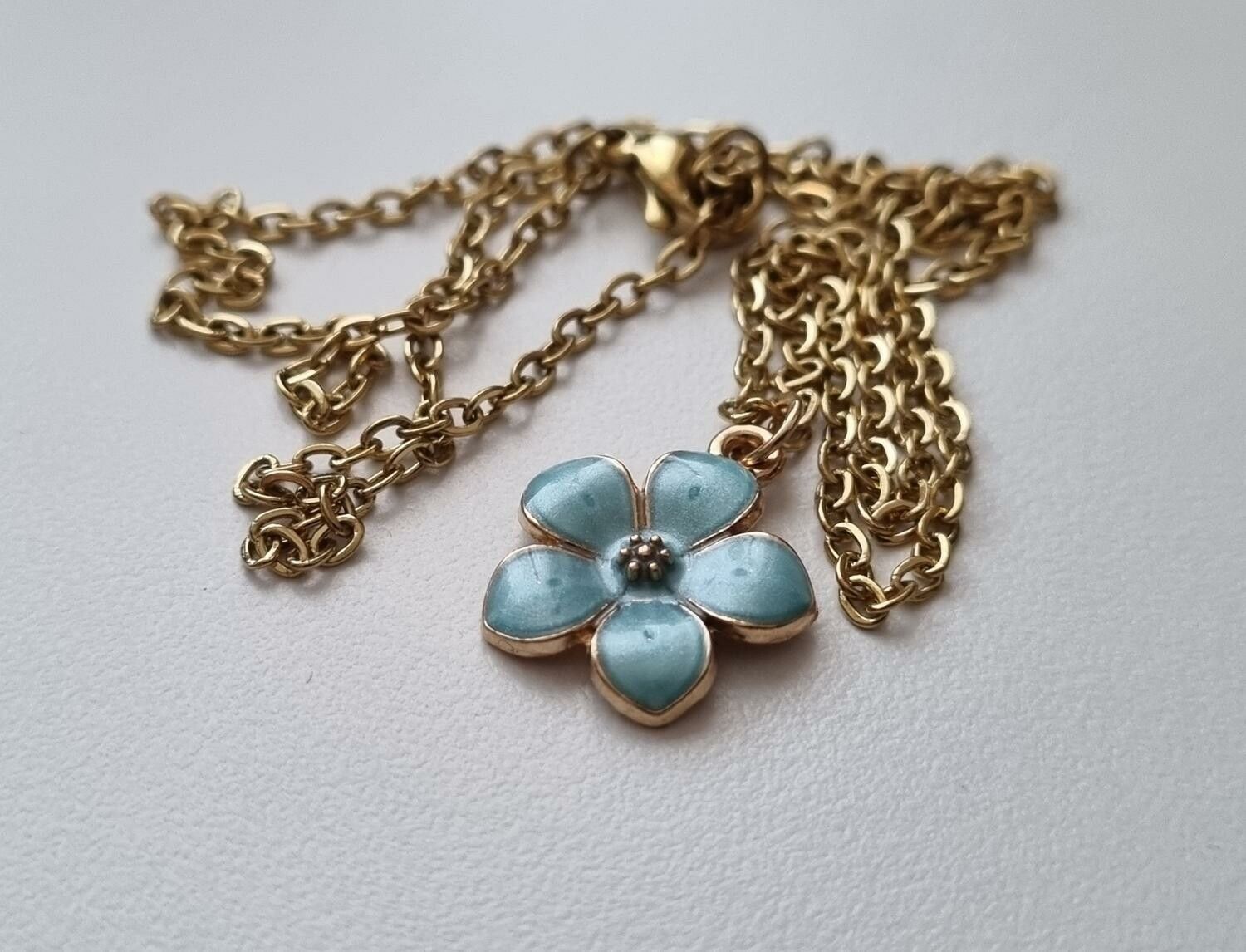 Guldfärgat halsband med en turkos blomma