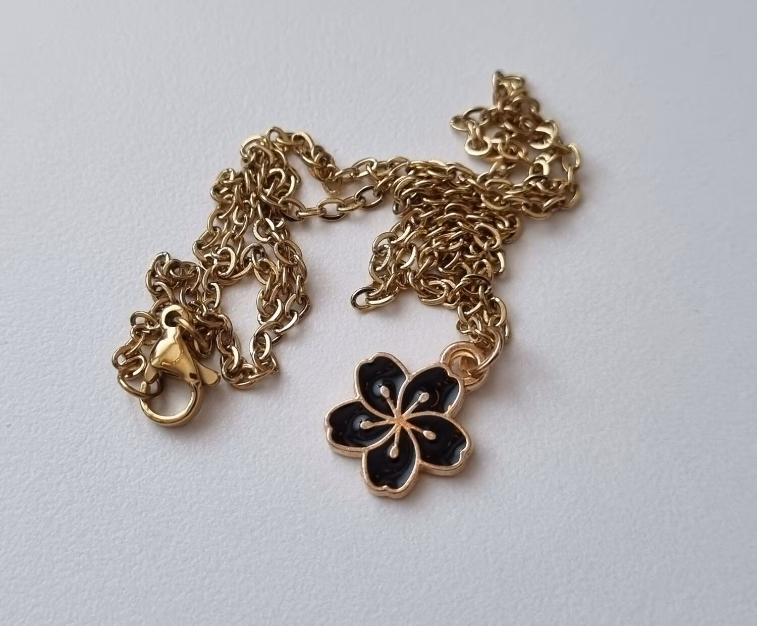 Guldfärgat halsband med en svart blomma