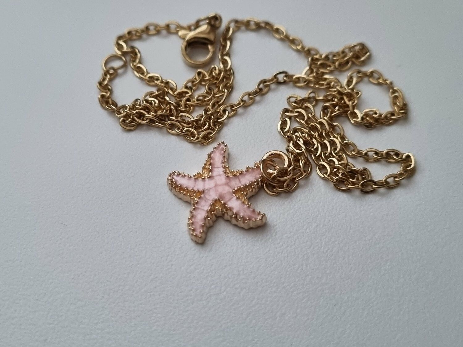 Guldfärgat halsband med en rosa sjöstjärna