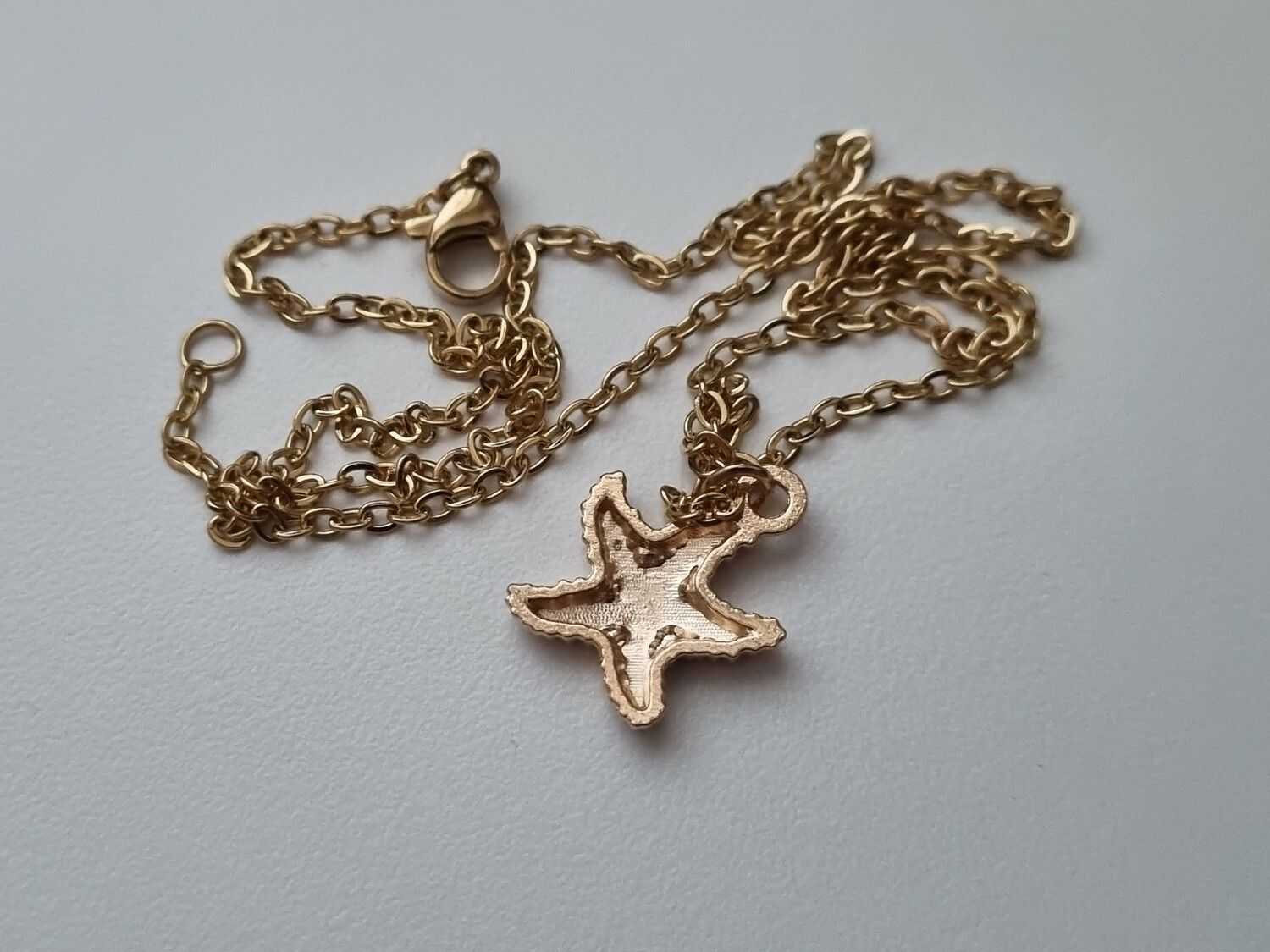 Guldfärgat halsband med en rosa sjöstjärna