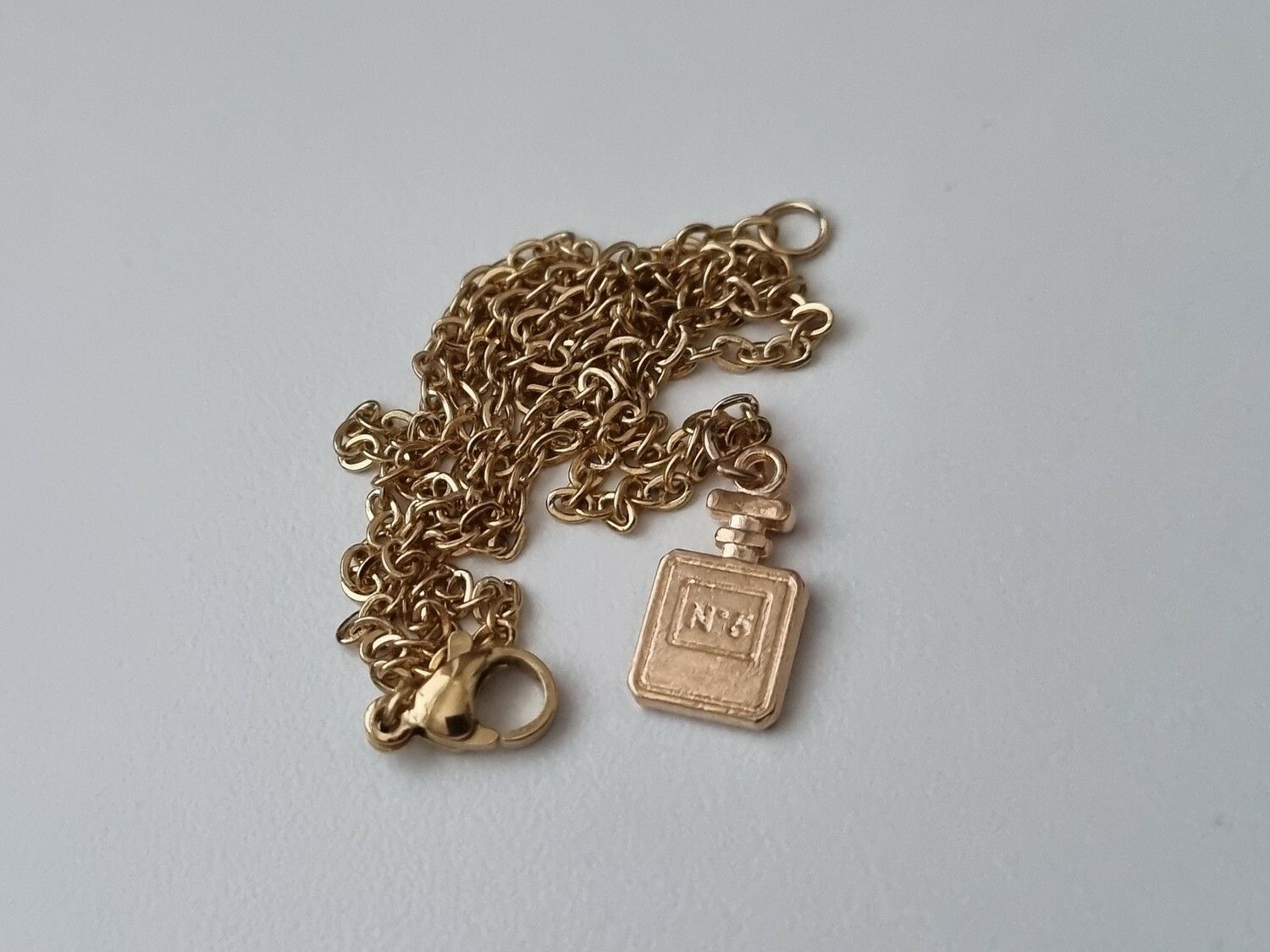 Guldfärgat halsband med en rosa parfymflaska