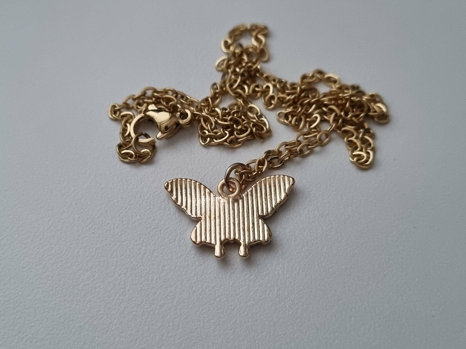 Guldfärgat halsband med en rosa fjäril