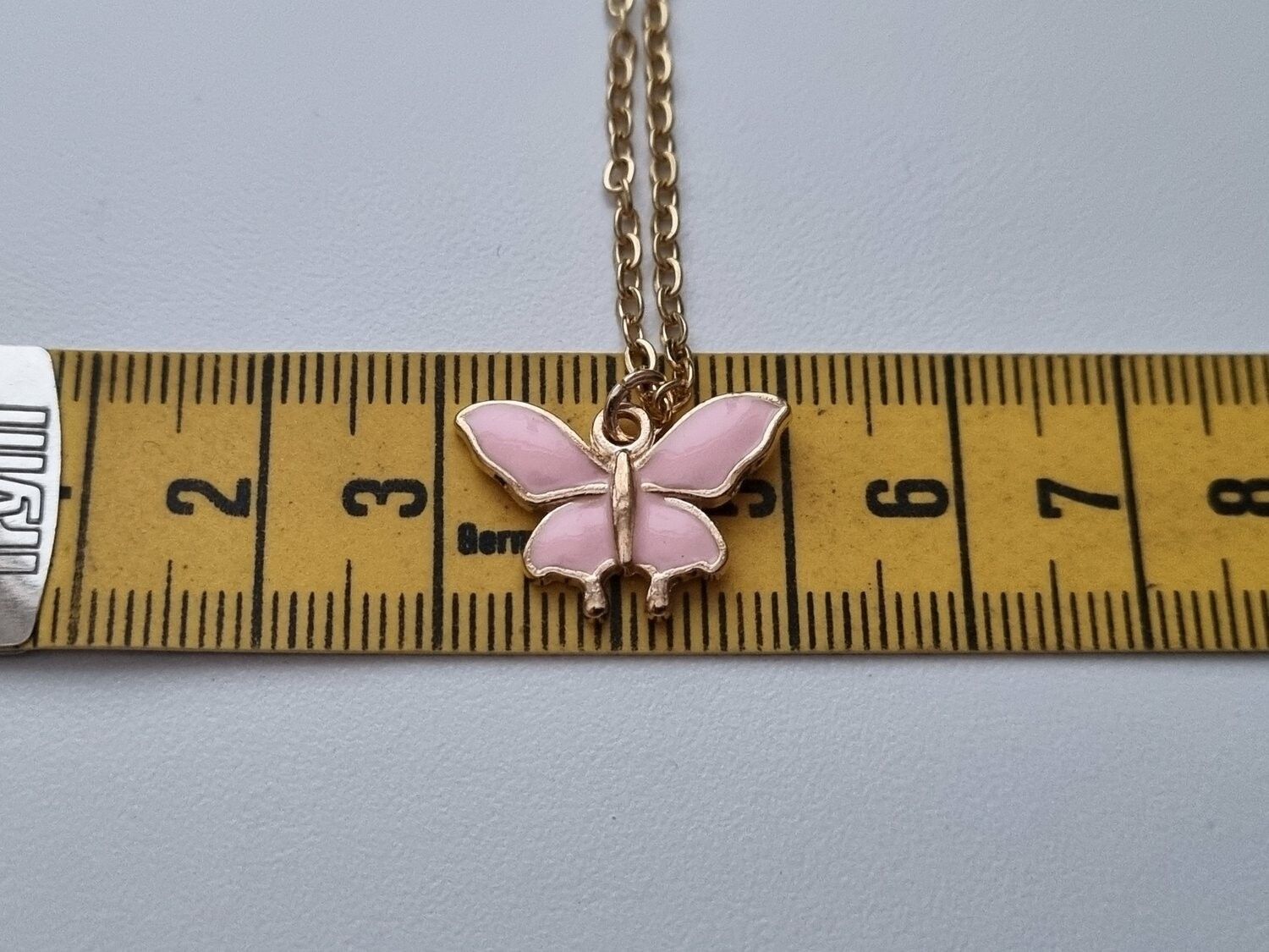 Guldfärgat halsband med en rosa fjäril
