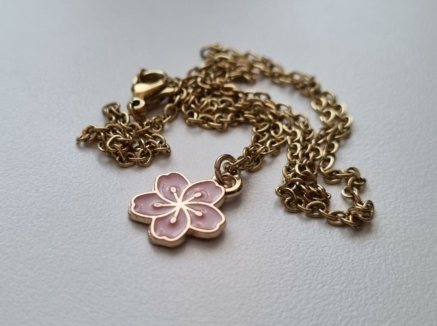 Guldfärgat halsband med en rosa blomma