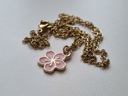 Guldfärgat halsband med en rosa blomma