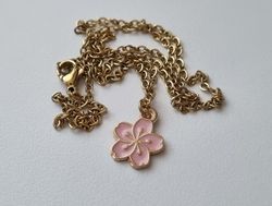 Guldfärgat halsband med en rosa blomma