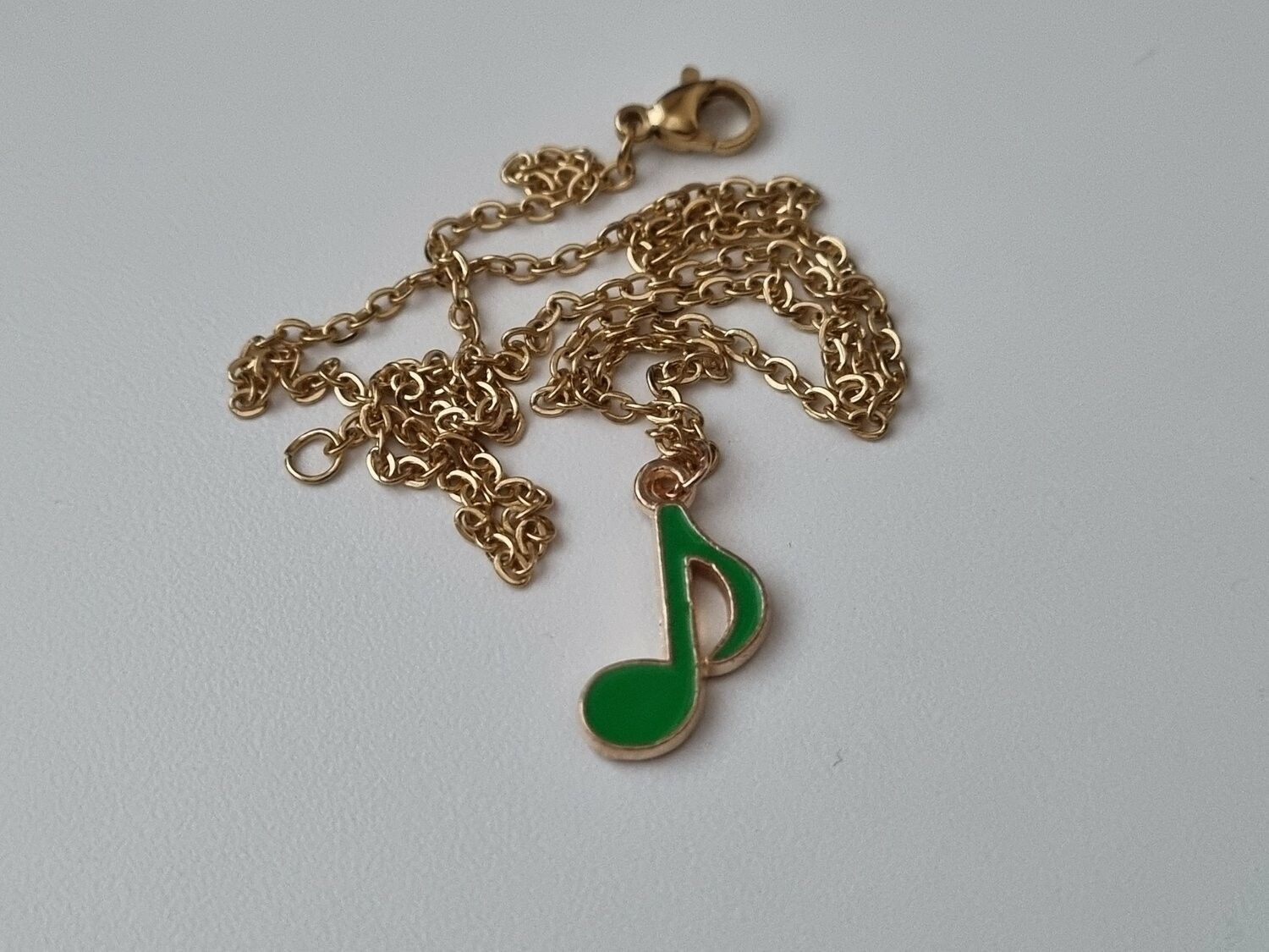 Guldfärgat halsband med en grön musiknot