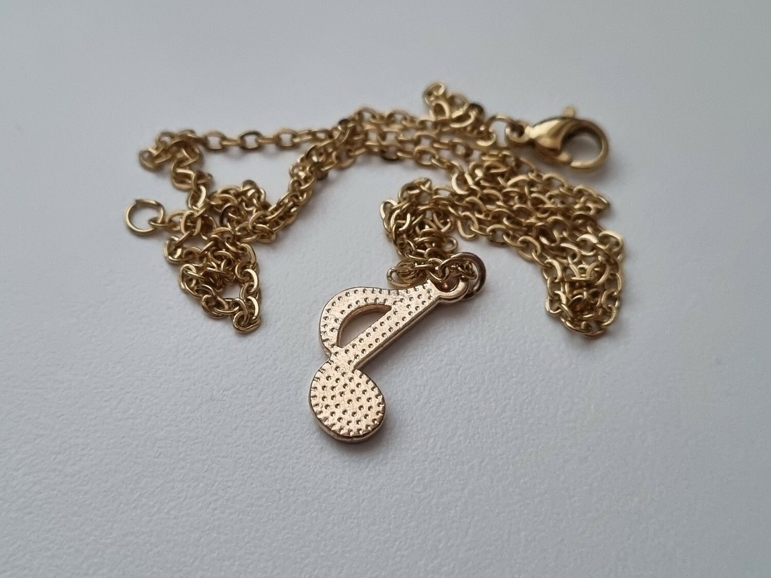 Guldfärgat halsband med en grön musiknot