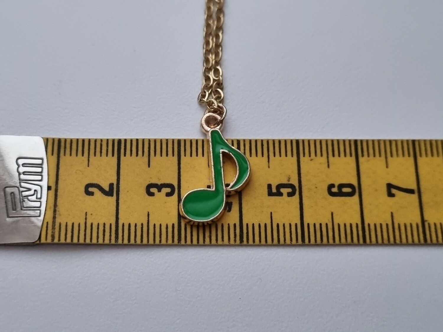 Guldfärgat halsband med en grön musiknot