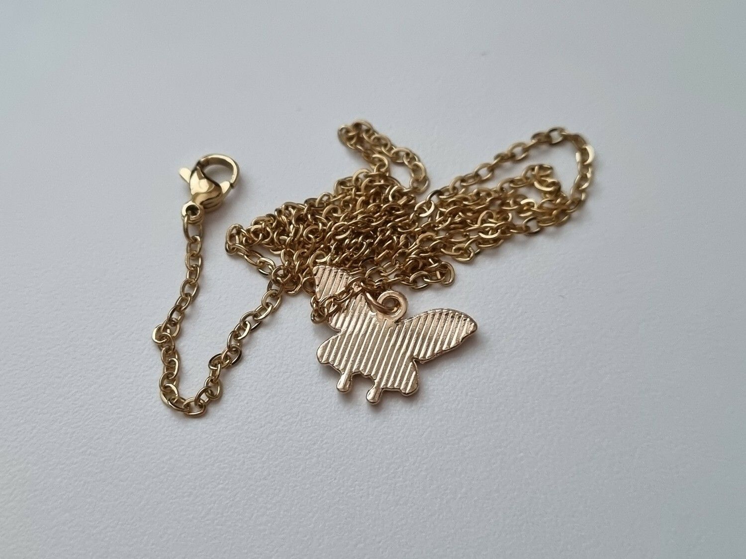 Guldfärgat halsband med en blå fjäril