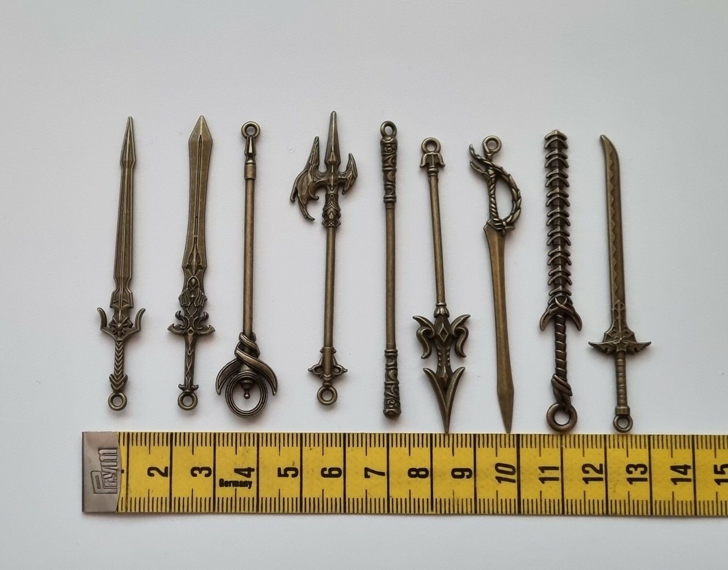 9 st berlocker - Miniatyrvapen, minisvärd, treuddar med mera (bronsfärgade)