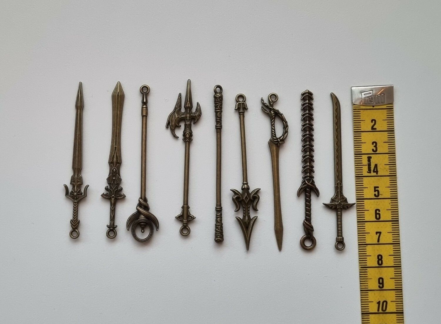 9 st berlocker - Miniatyrvapen, minisvärd, treuddar med mera (bronsfärgade)