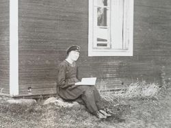 Vykort bild på person som läser bok framför en stuga.