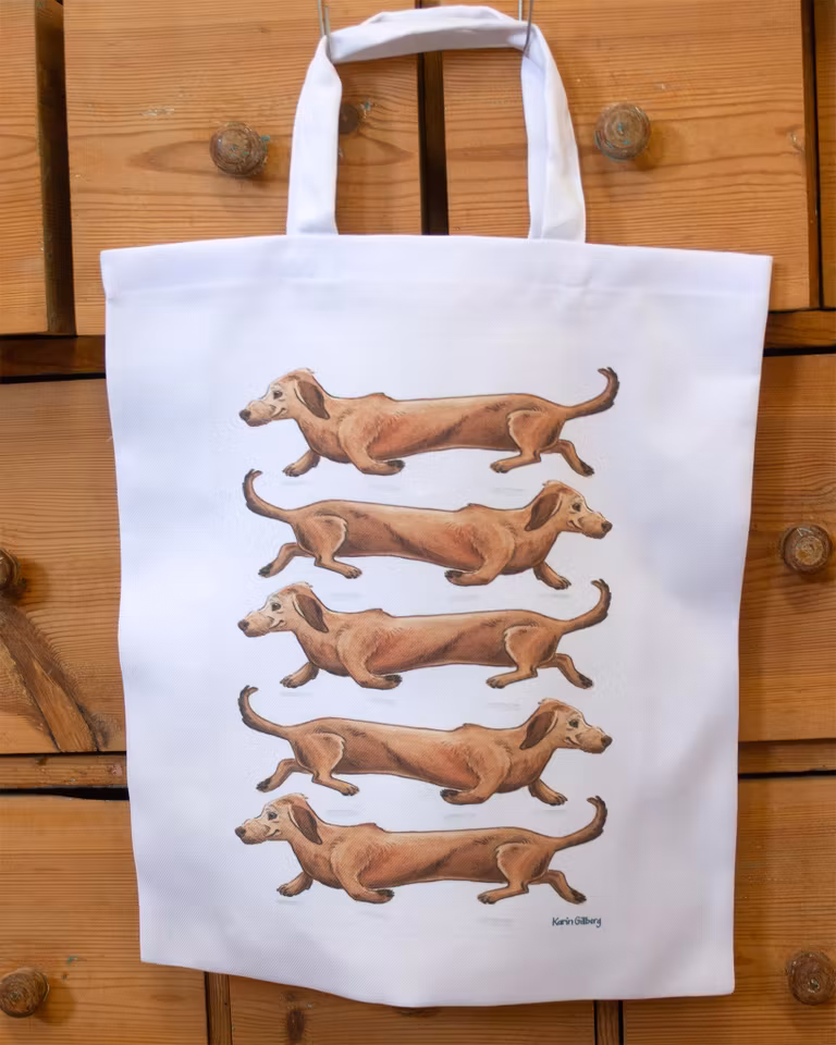 Kasse i tyg med motiv av fem långa taxar. Kassen kan du ha med i ryggsäcken, redo att användas till shoppingturen.