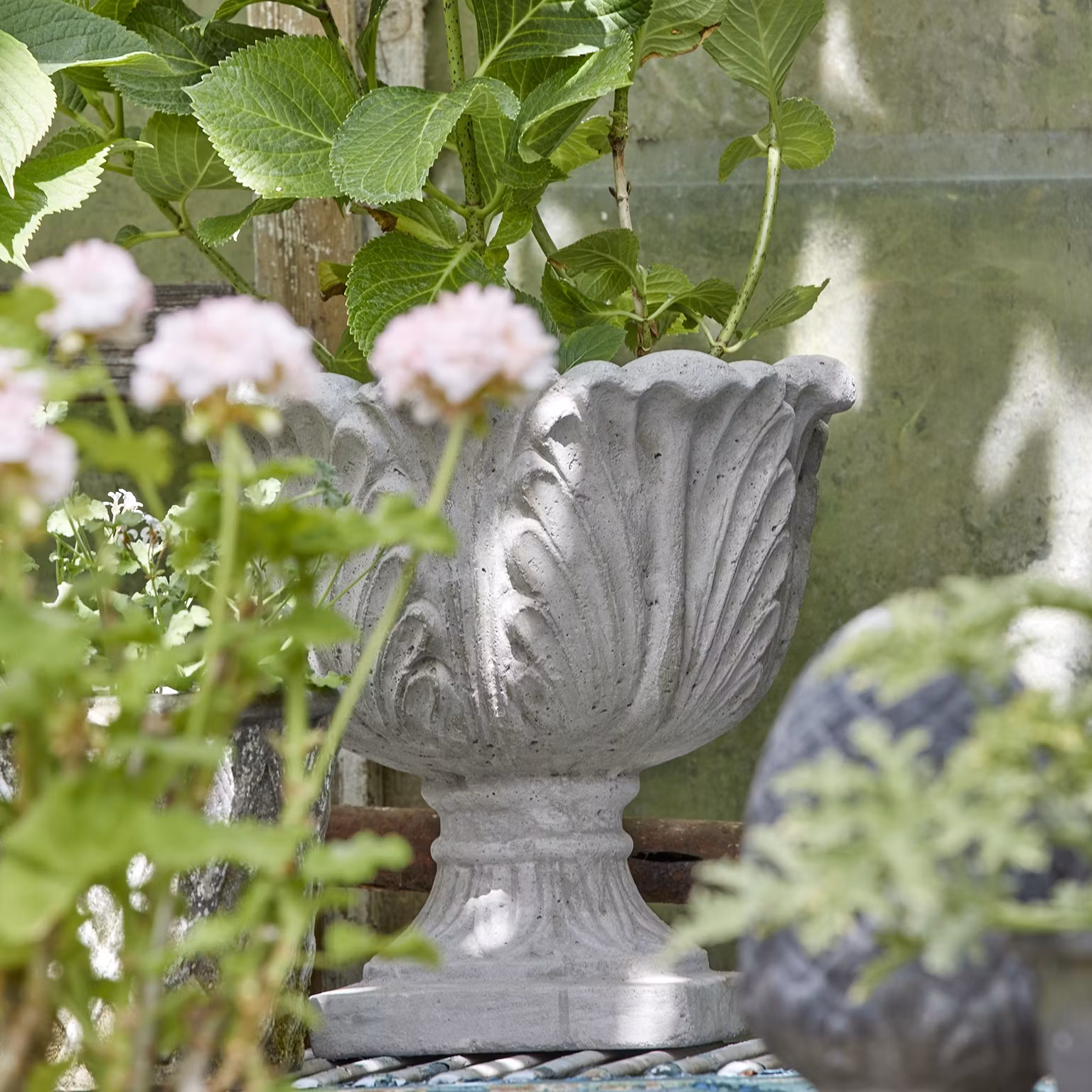 Kruka på fot i grov betong med dekorativa blad