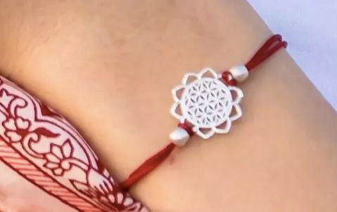 Armband med livets blomma-motiv i mässing. Justerbart band av mörkröd bomull. Fair Trade från Indien. Dekorationsbild.