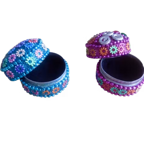 Två små glittriga nipperaskar i turkos och lila dekorerade med små blommor. Med öppet lock, det svarta fleecefordret syns. Fair Trade Indien.