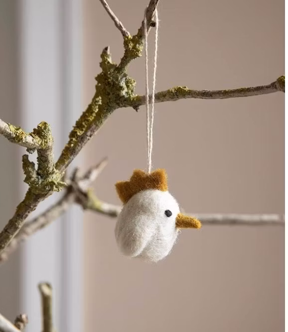 En liten kyckling i vit med gul kam som påskhänge. Bild med deko.