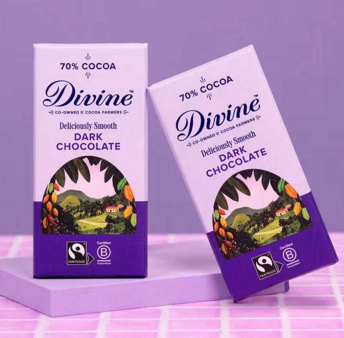 Divine Mörk choklad 70%, Fairtrade, Kakao från Ghana. Vegansk. Dekorationsbild med två kakao mot lila bakgrund.