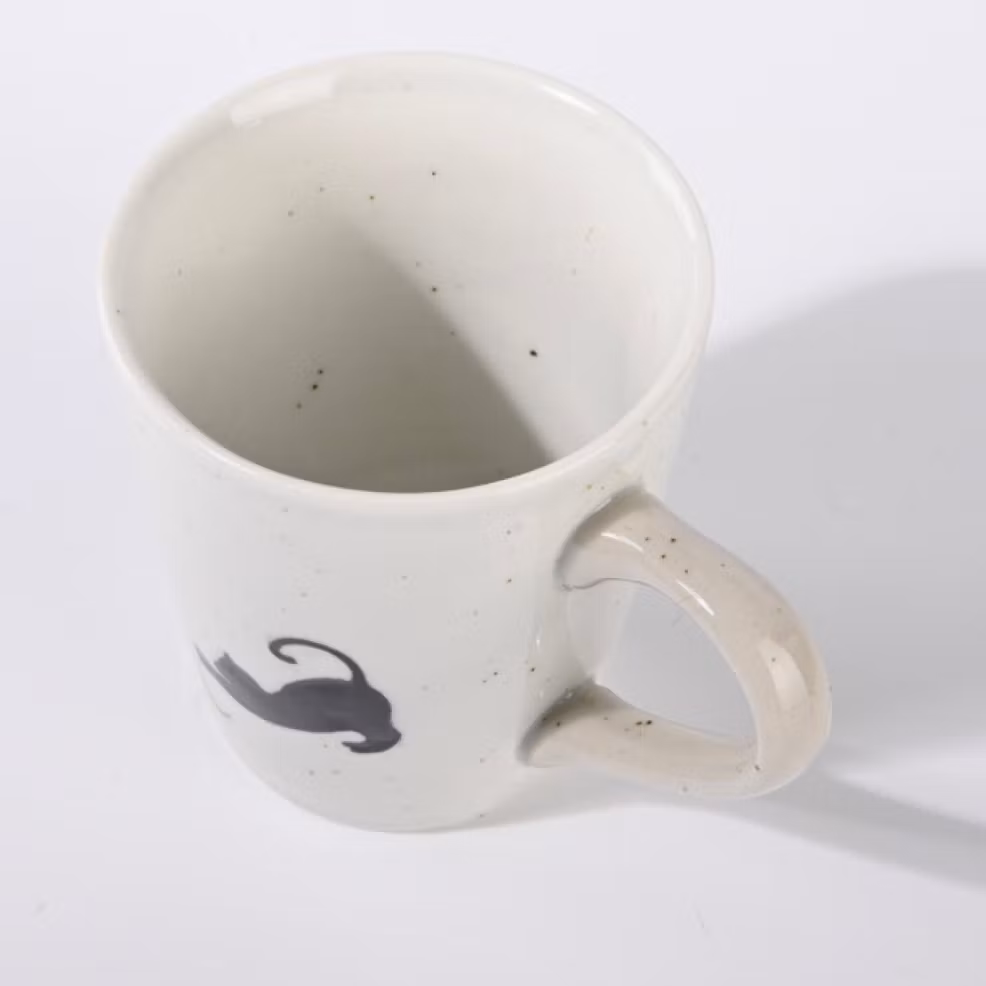 En beige-vit kopp till kaffe, te eller varm choklad. Motivet är en liten svart katt som leker med ett garnnystan, keramik. Fair Trade.
