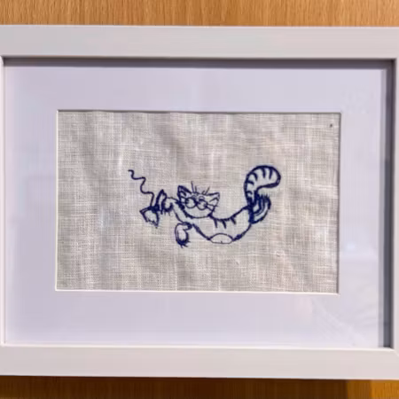Broderad tavla med en katt som leker. Välj färg på brodyren
