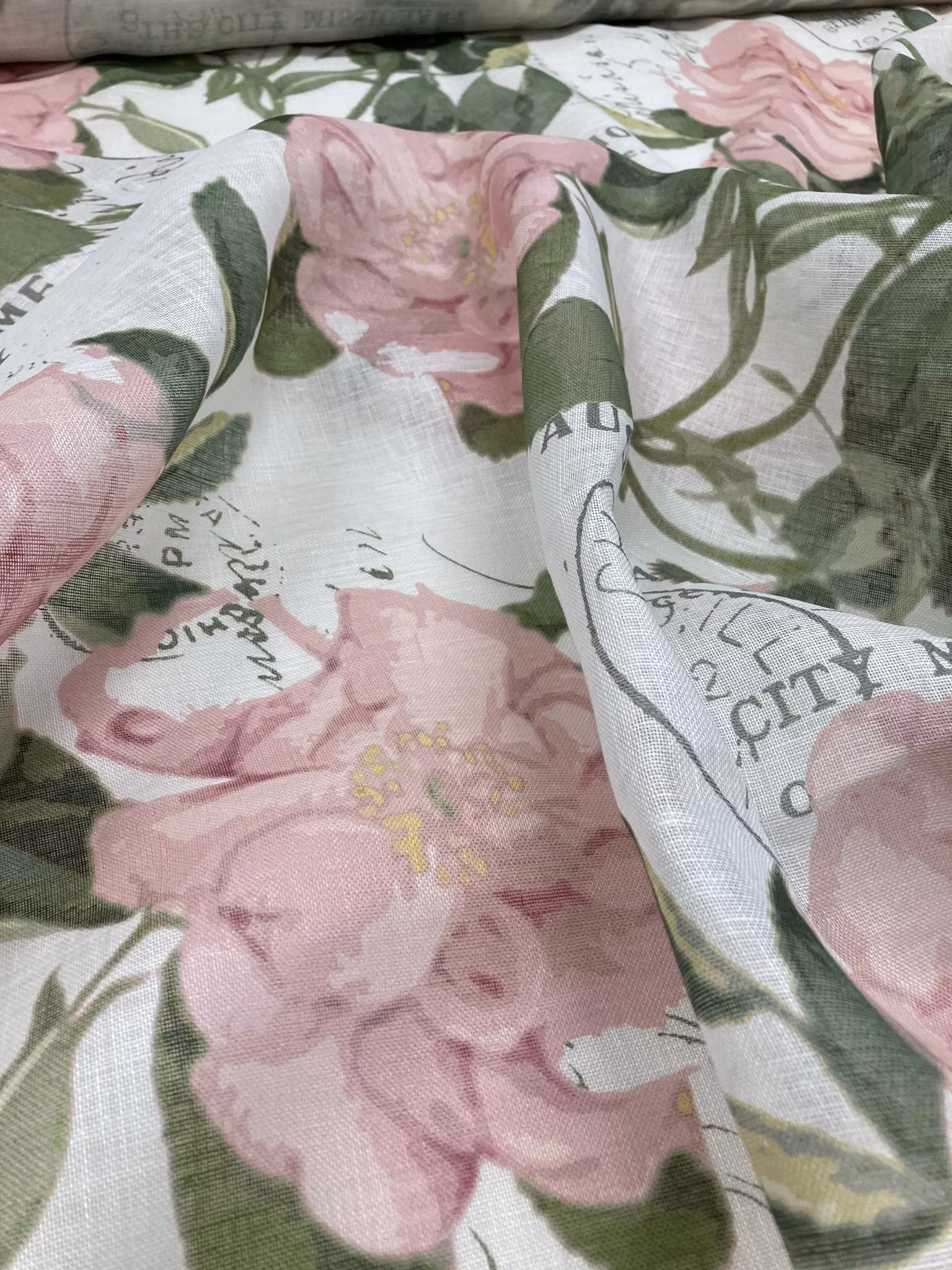 Ljust linnetyg med rosa nyponrosor, gröna blad och vintageinspirerade poststämplar på vit botten.