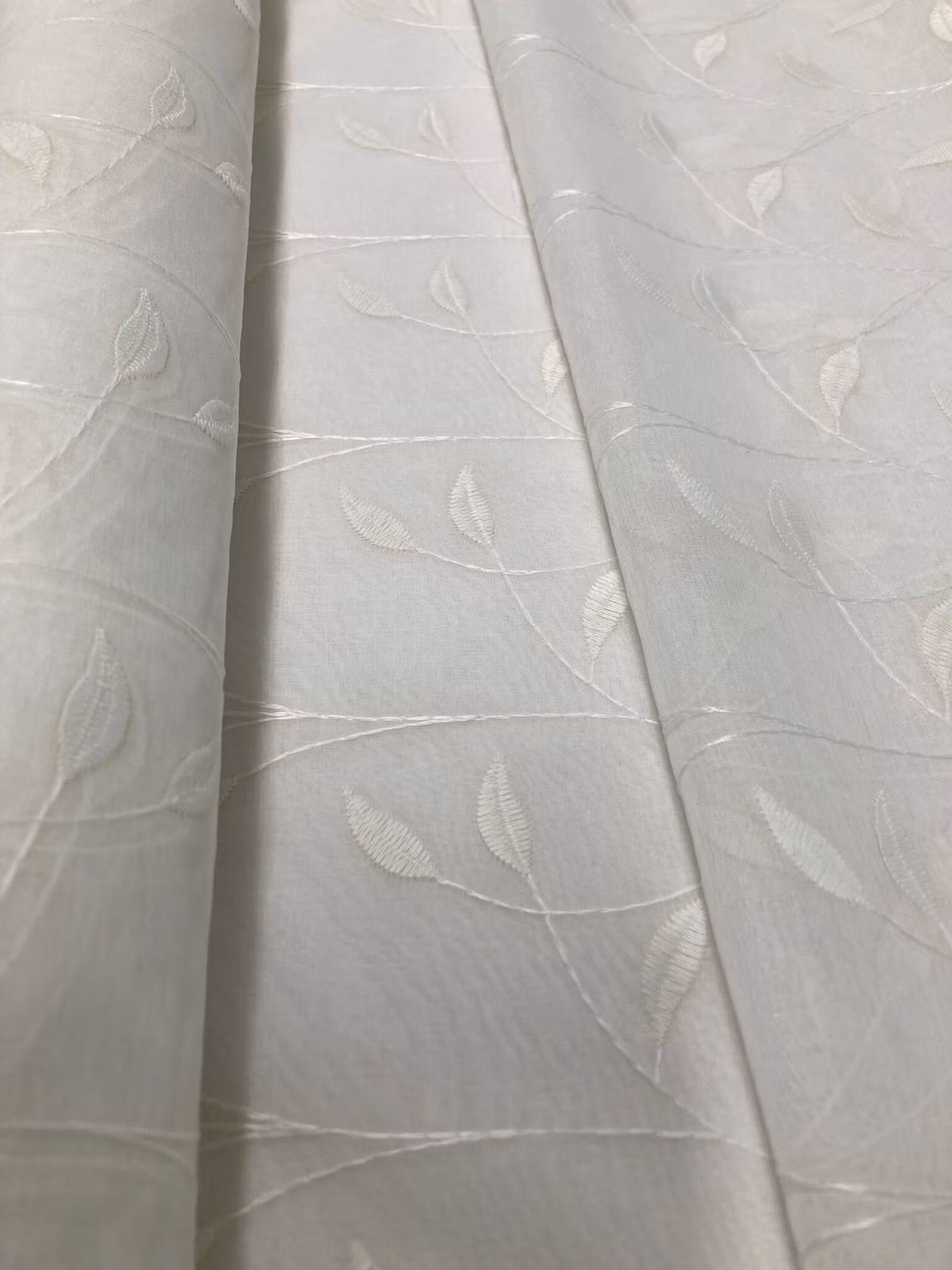 metervara med vackert broderade bladslingor på transparent botten