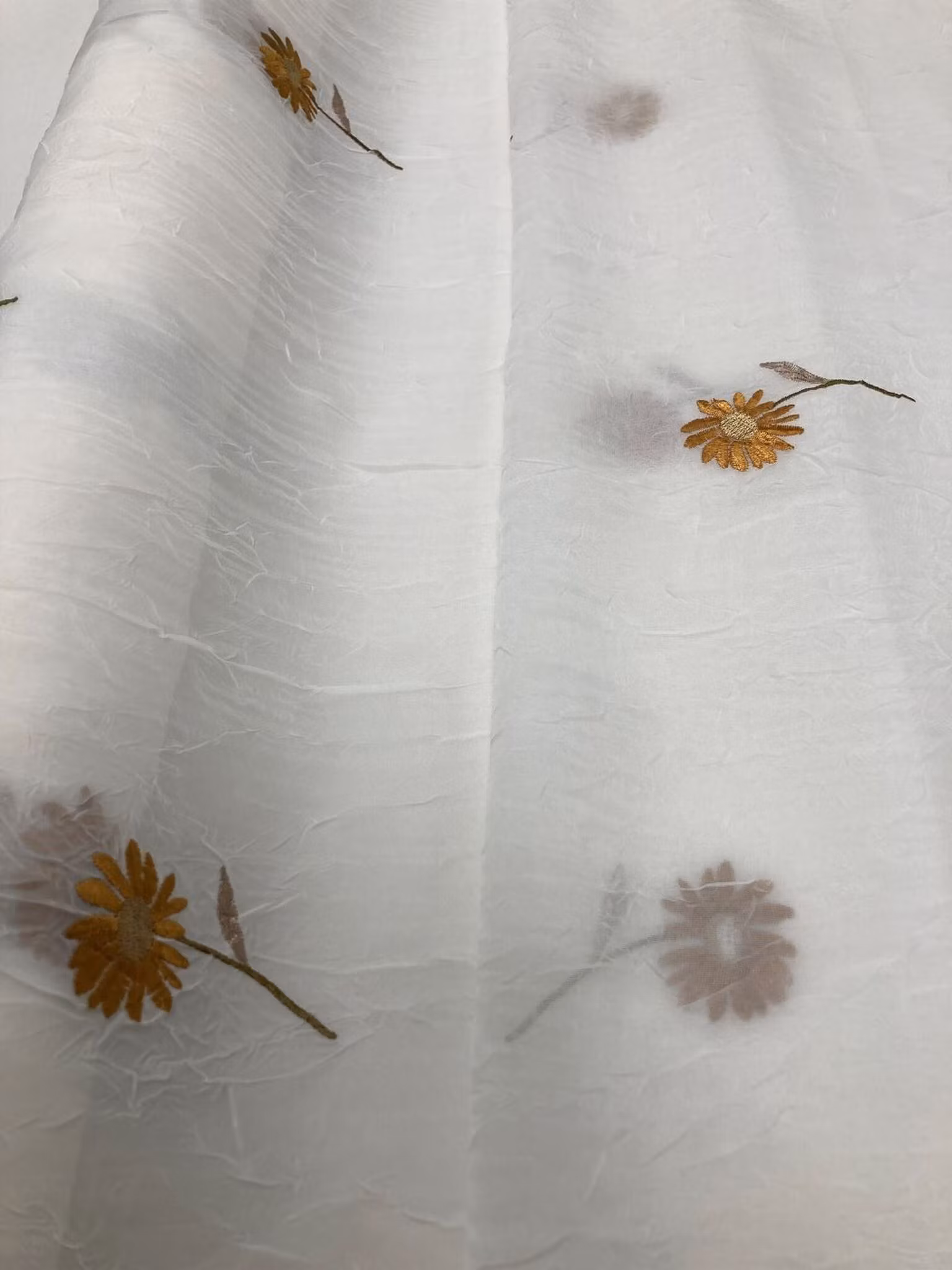 gardinmetervara med vackra broderade blommor i varma ockragula toner