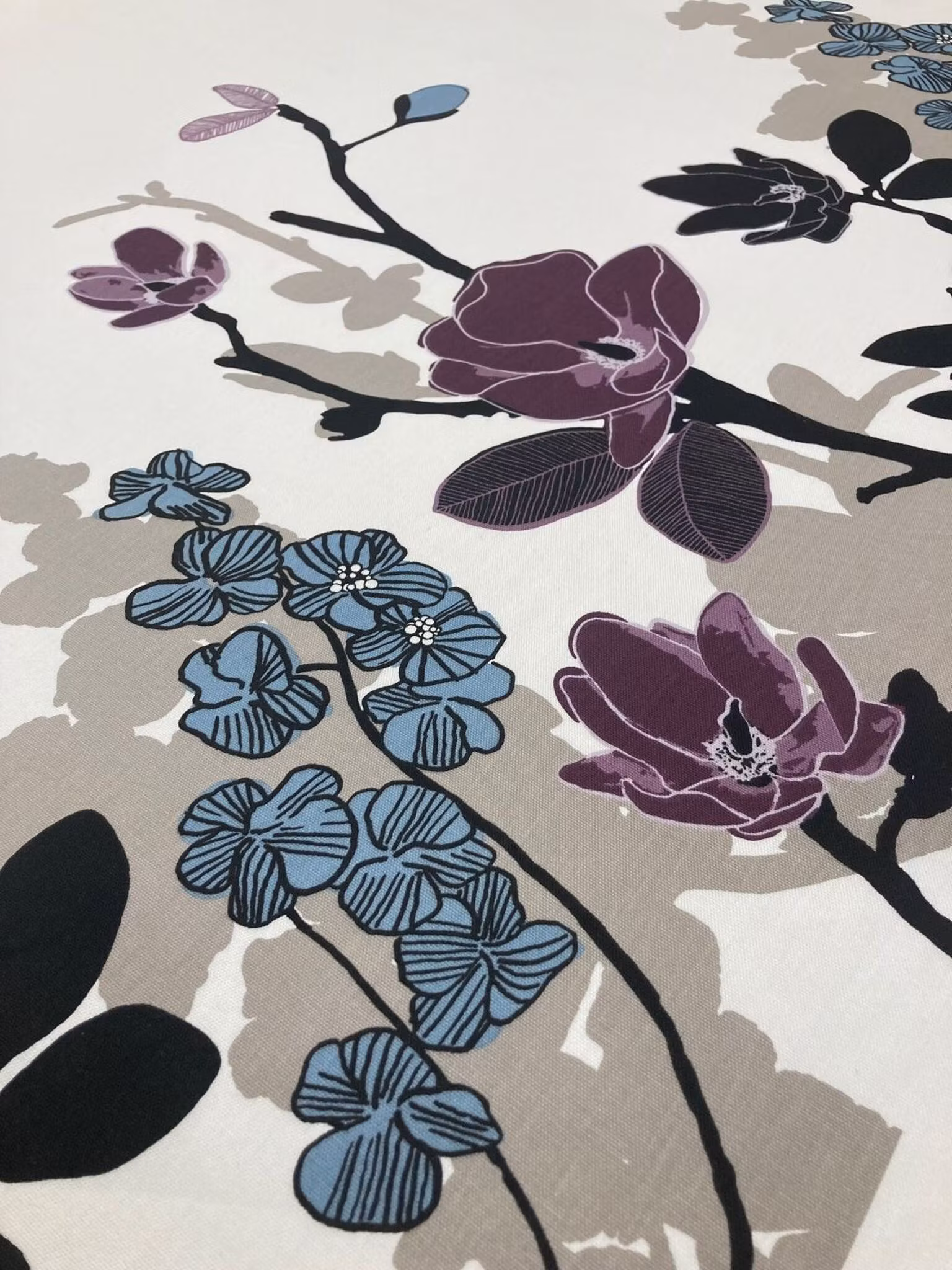 Närbild av Grandiflora multi med blå och plommonlila magnoliablommor, svarta grenar och tydlig tygstruktur.