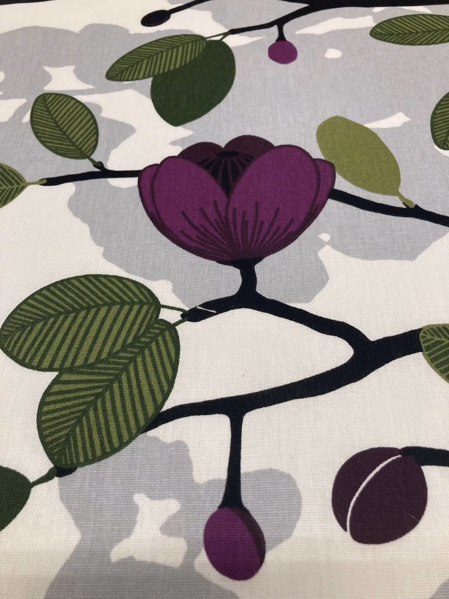 Närbild av Ofelia som visar blommotivet med plommonfärgade blommor och gröna blad på ljus botten.