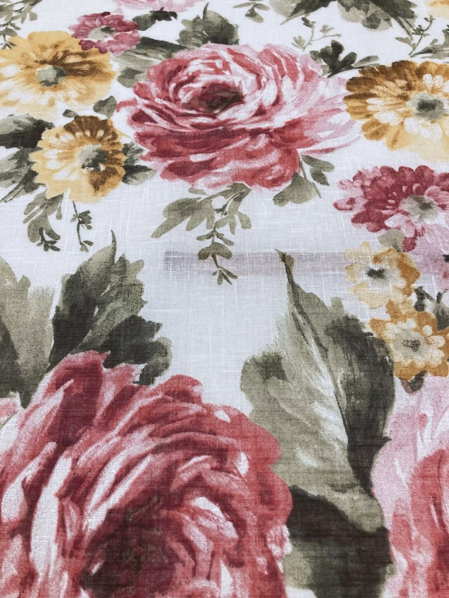 Närbild av Diblujo gardintyg med rosor, gröna blad och mindre blommor på ljus botten.