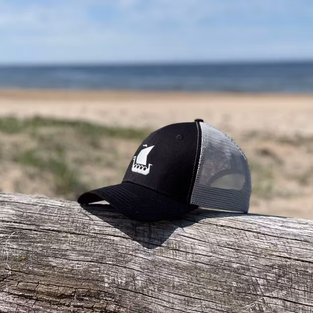 A Mesh Cap Black and Grey from TAC-UP GEAR seen from the side front on a log on a beach