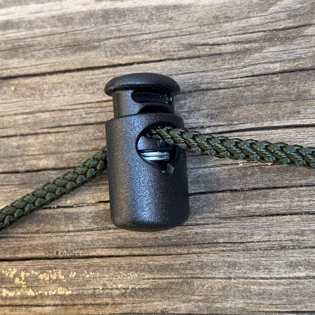 Cord Lock Shiny Black photo with green string through it laying on a wooden floor