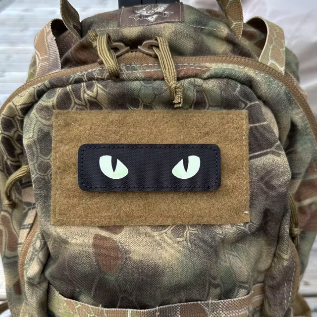 Glow Eyes Patch mounted on a camouflage backpack in daylight