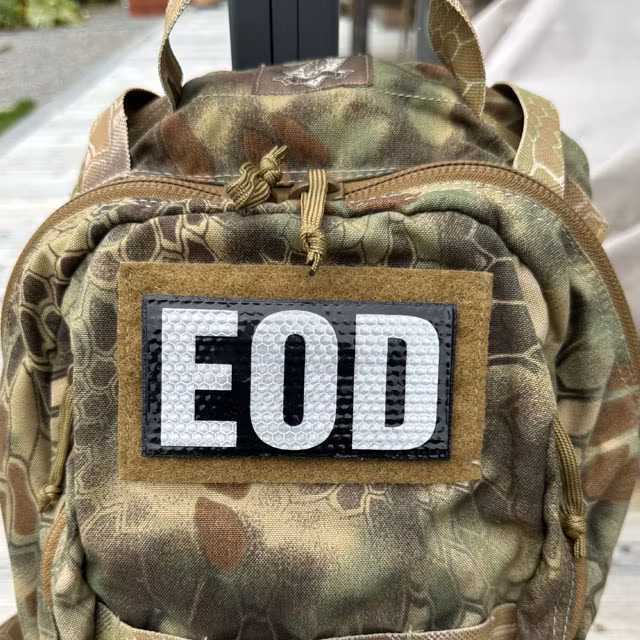 IR EOD Reflective Black & White Hook Patch mounted on a camouflage backpack