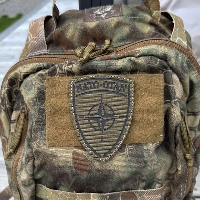 IR-NATO Shield Reflective Green Hook Patch mounted on a camouflage backpack