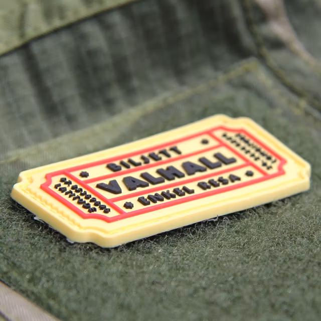 Ett Biljett Valhall PVC Gul/Röd monterat på ärmen på en Field Shirt M90.