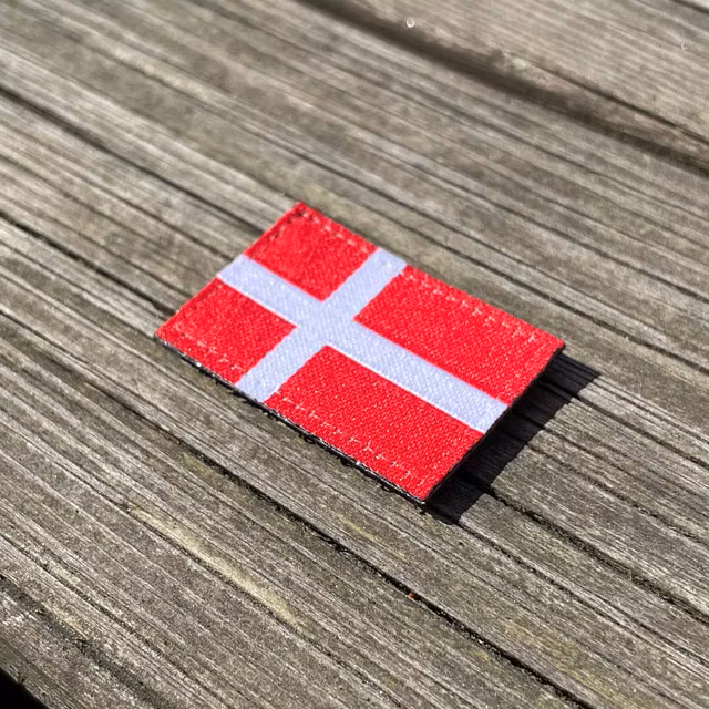 Denmark Flag Hook Patch Small from TAC-UP GEAR lying flat on wood seen from an angle