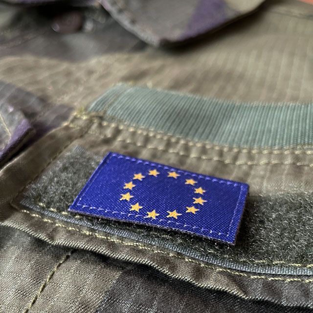 A Blue and yellow EU Flag Hook Patch Small from TAC-UP GEAR on a M90 Shirt seen from an angle