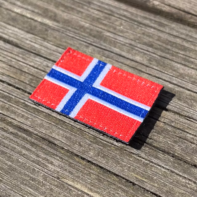 A Norway Flag Hook Patch Small from TAC-UP GEAR lying flat on wooded plank seen from an angle
