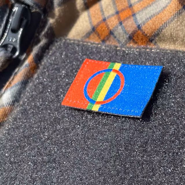 A close up picture of a Sámi Flag Hook Patch Small from TAC-UP GEAR mounted with hook and loop on a shirt sleeve