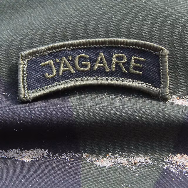 M90 camouflage background and a JÄGARE Patch Green/Black/Green M14.