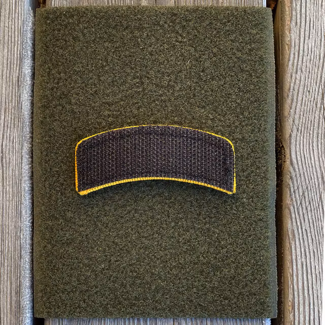 A JÄGARE Hook Patch Orange/Black face down on a pice of green loop fabric showing the hook backing in black